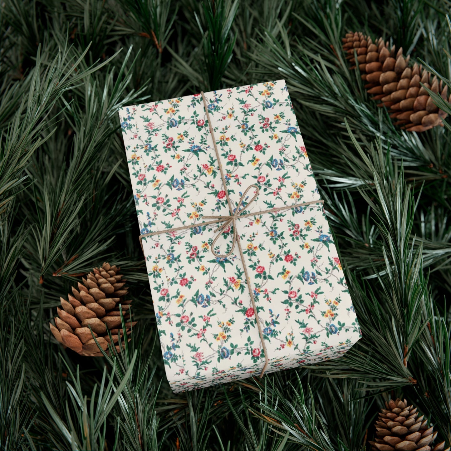 Gift box wrapped in floral paper with string, surrounded by pine branches and cones.