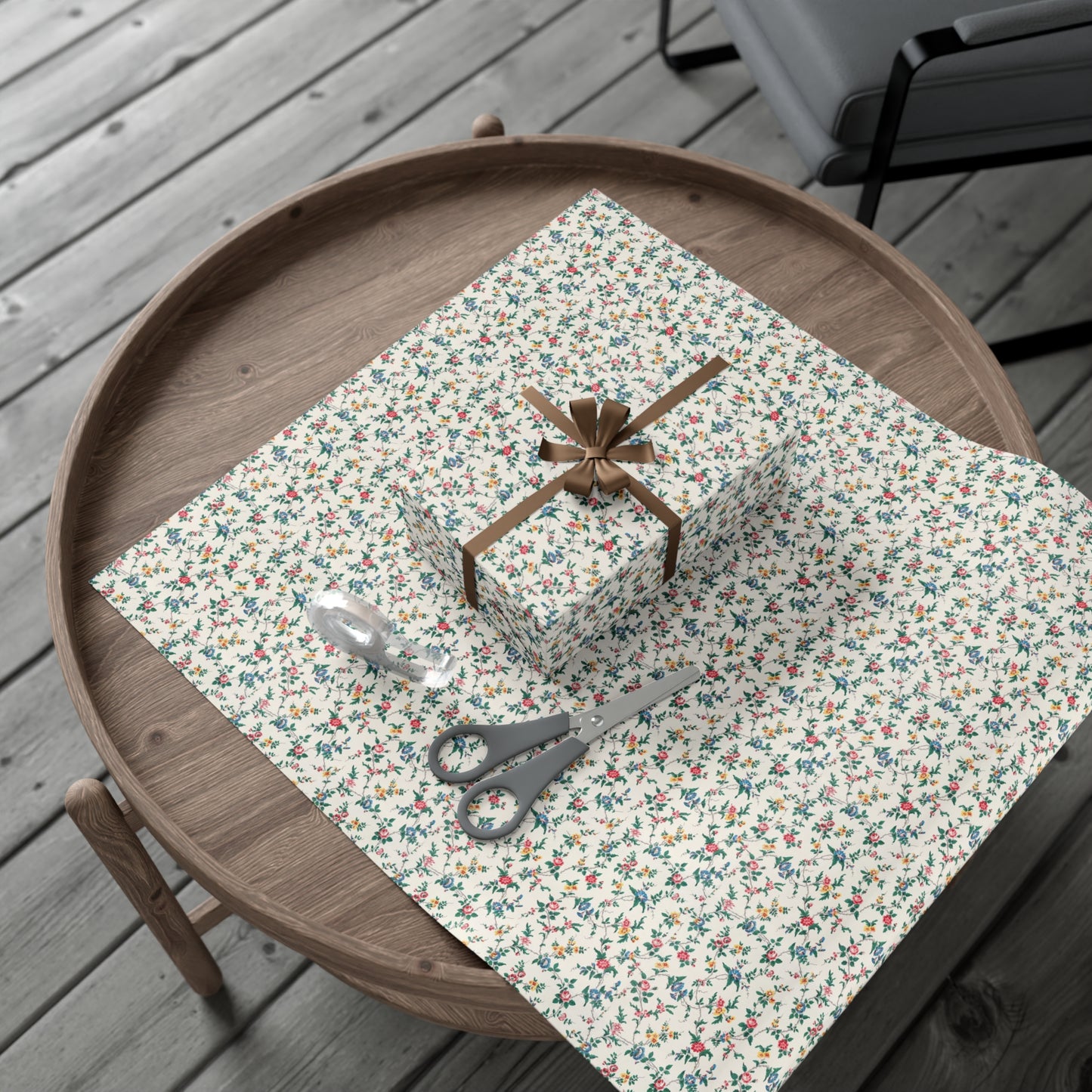 Floral-patterned tablecloth on a wooden tray with a gift and scissors on a wooden surface.